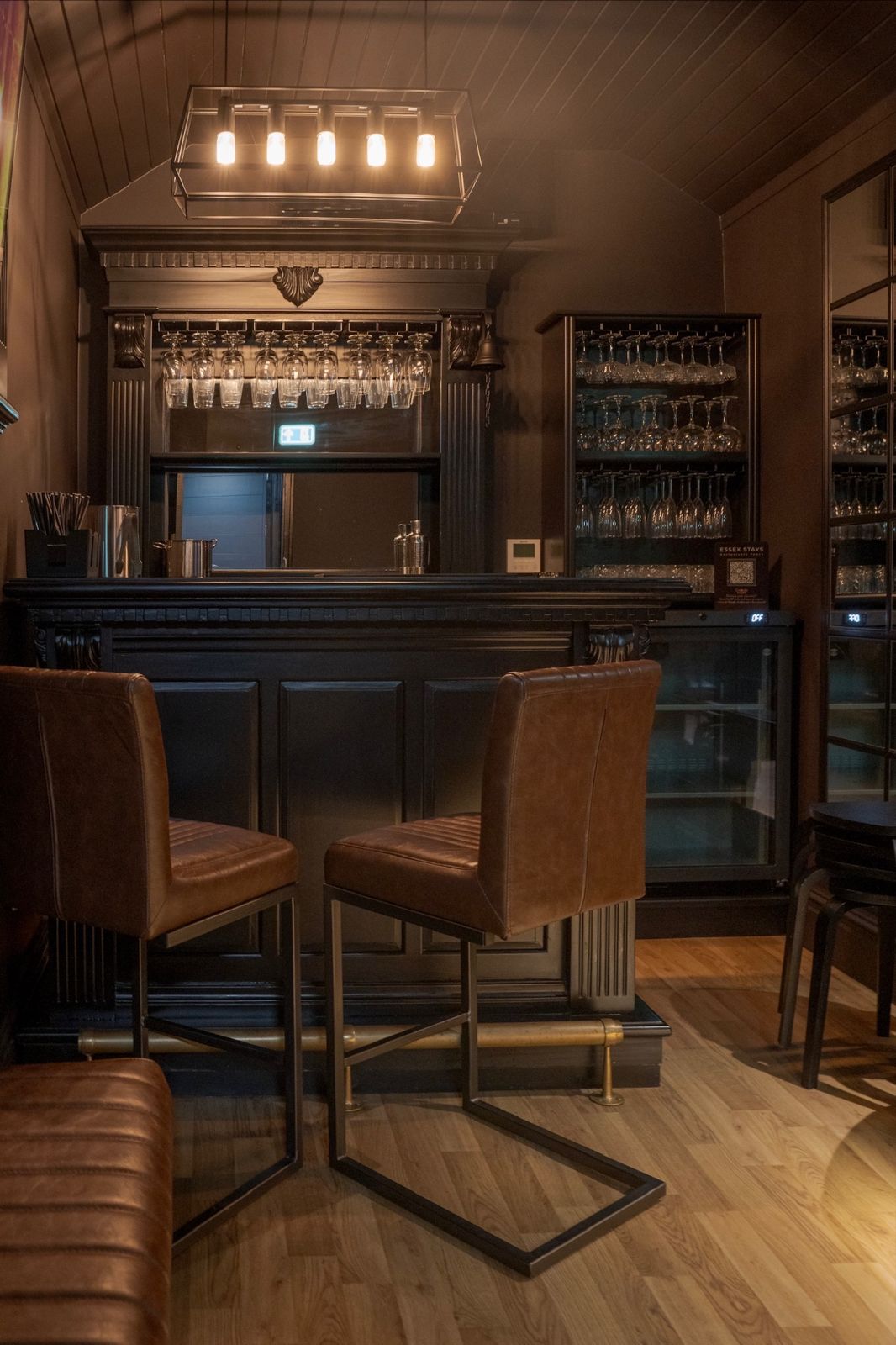 Private cocktail bar with carved black back bar, hanging glassware and tan leather stools
