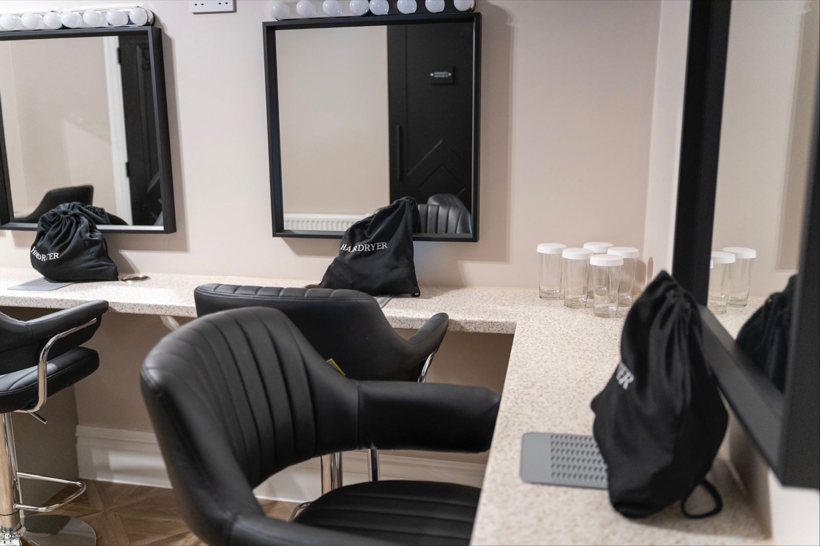 Vanity Room with lit mirrors, stools and hairdryers